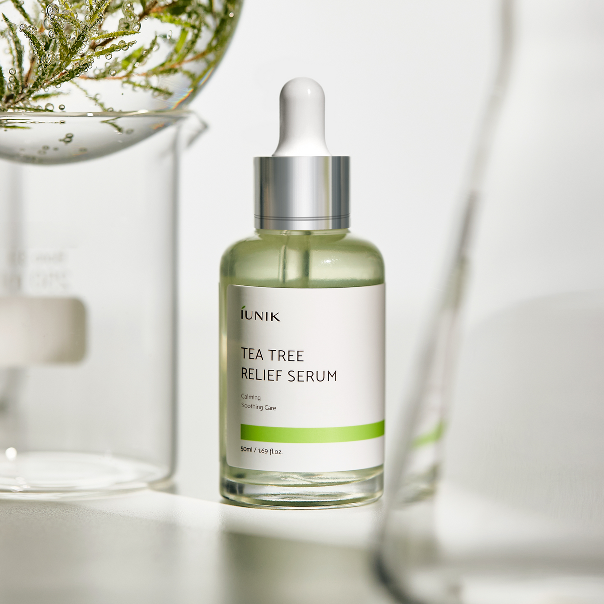 IUNIK Tea Tree Relief Serum - butelka wśród szklanych naczyń laboratoryjnych i gałązki | Ellemania
