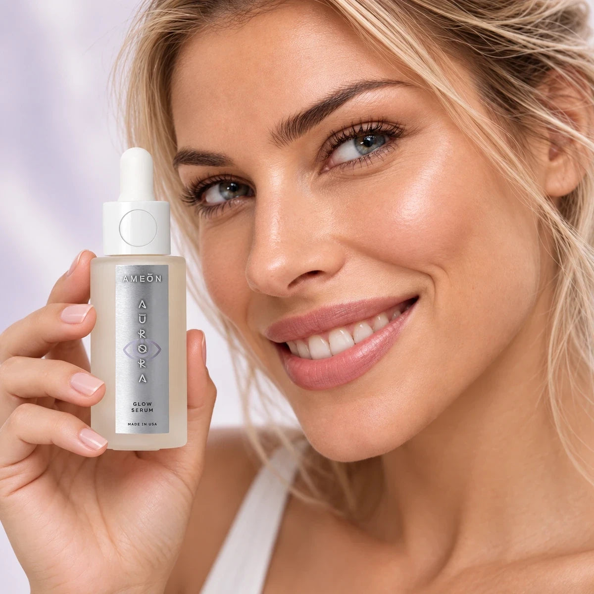 AMEON Aurora Glow Serum 30 ml, uśmiechająca się kobieta trzymająca szklaną butelkę z pipetą przy twarzy | Ellemania
