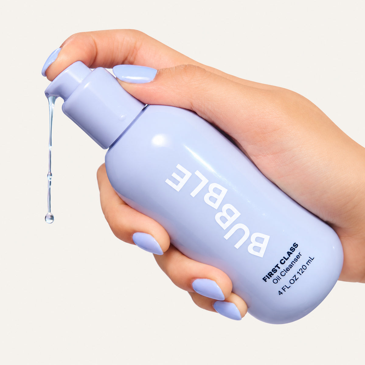 Bubble First Class Oil Cleanser 120 ml, hand with lavender nails holding a pump bottle with oil dripping from it | Ellemania
