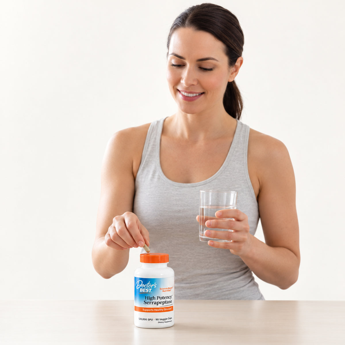 Doctor's Best High Potency Serrapeptase 90 kapsułek, kobieta z butelką suplementu na blacie i szklanką wody | Ellemania