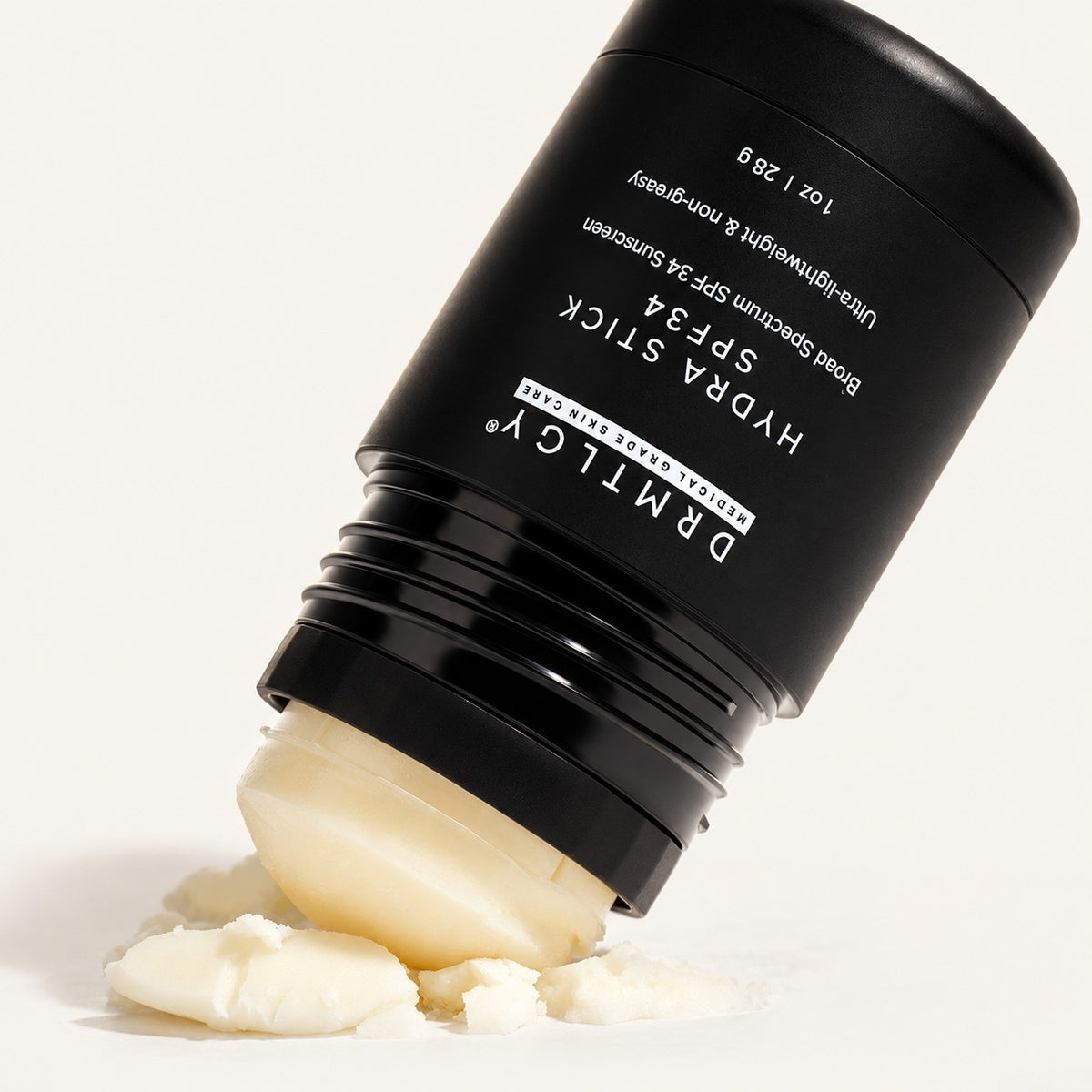 DRMTLGY Hydra Stick SPF 34, 28 g - czarny sztyft z odsłoniętą jasną masą oparty o rozkruszone fragmenty produktu | Ellemania