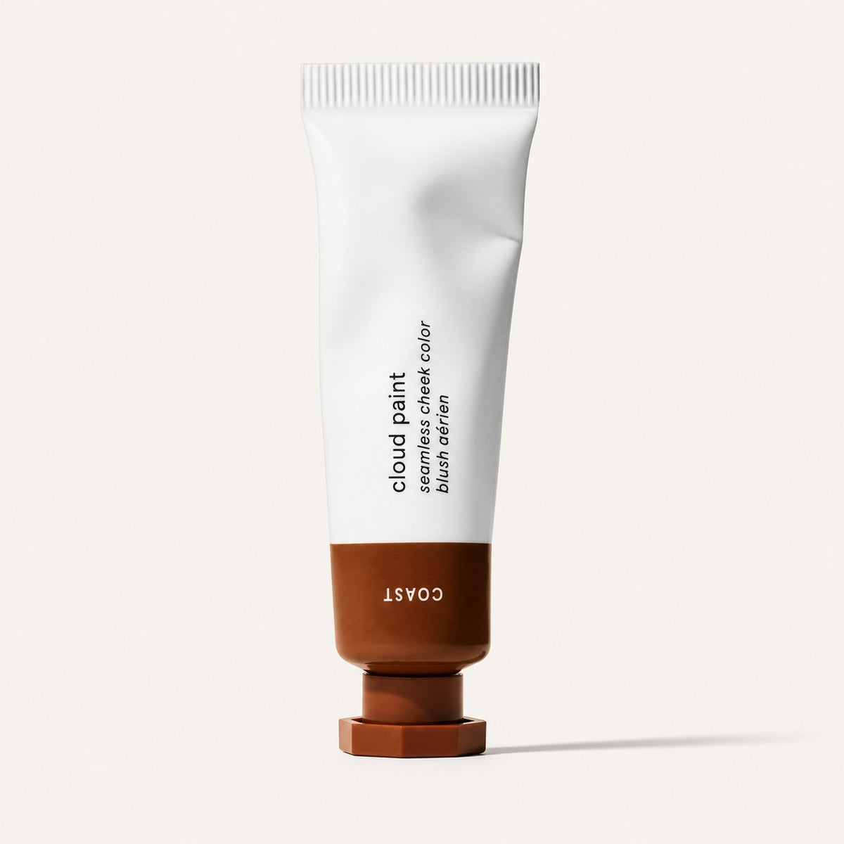 Glossier Cloud Paint - odcień Coast, biała tubka z brązową końcówką i nakrętką, na opakowaniu napis Coast, jasne tło | Ellemania