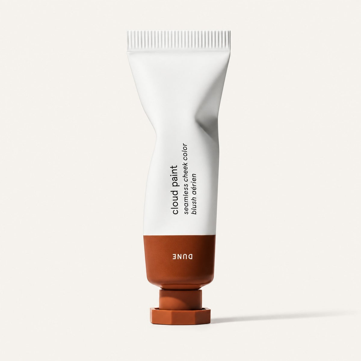 Glossier Cloud Paint - odcień Dune, skręcona biała tubka z rudobrązową końcówką i nakrętką, na opakowaniu napis Dune, jasne tło | Ellemania