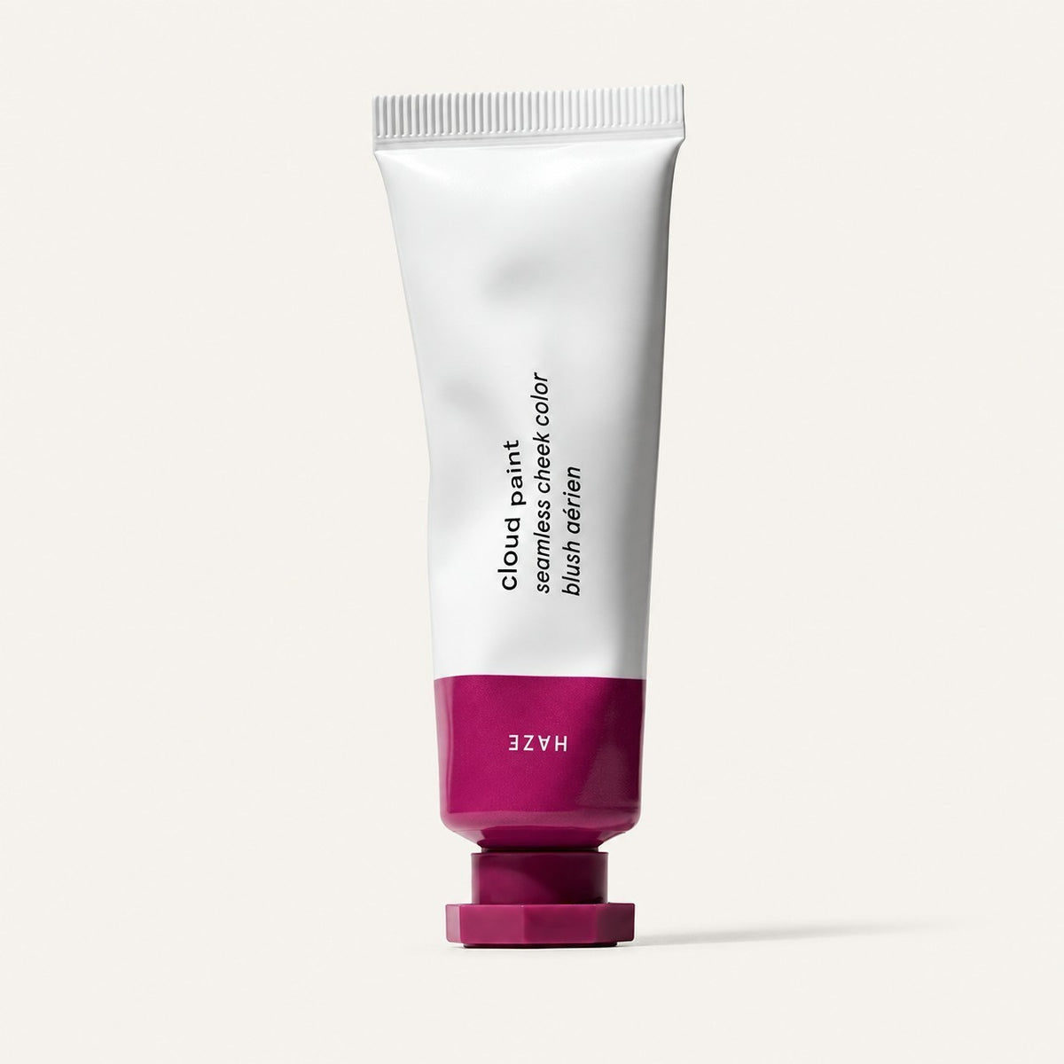 Glossier Cloud Paint - odcień Haze, biała tubka z purpurowo-fuksjową końcówką i nakrętką, na opakowaniu napis Haze, jasne tło | Ellemania