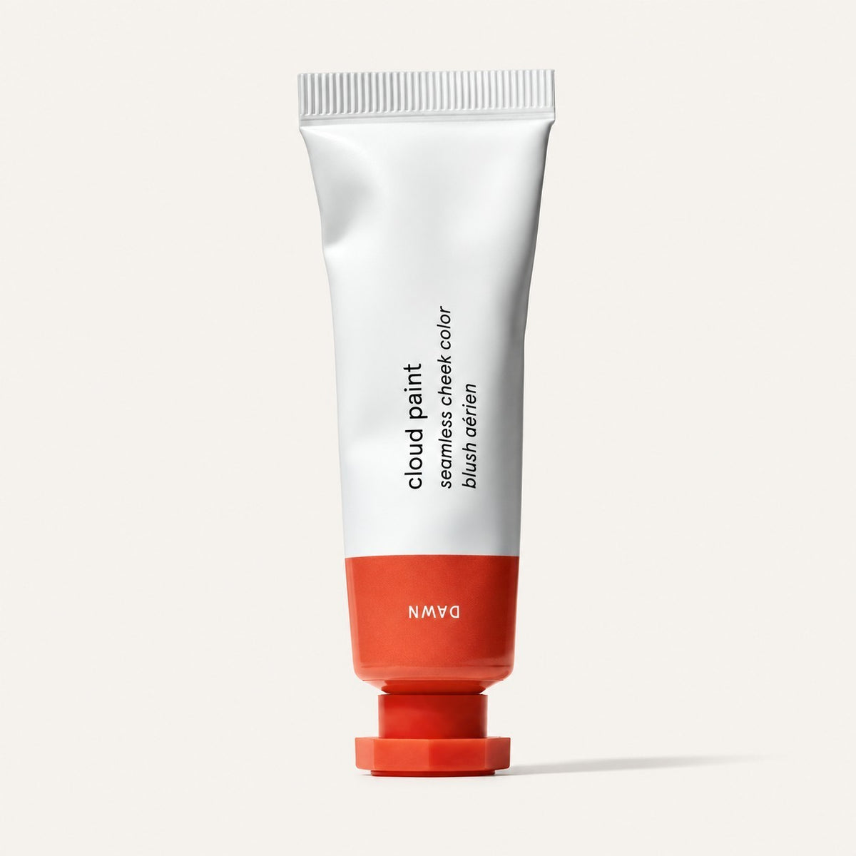 Glossier Cloud Paint - odcień Dawn, biała tubka z czerwonopomarańczową końcówką i nakrętką, na opakowaniu napis Dawn, jasne tło | Ellemania