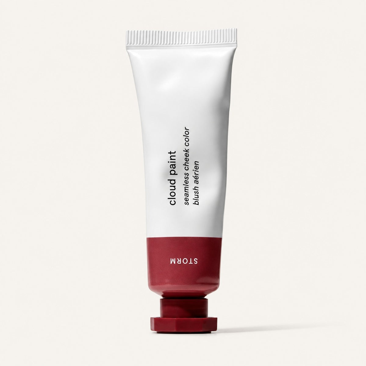 Glossier Cloud Paint - odcień Storm, biała tubka z ceglastobordową końcówką i nakrętką, na opakowaniu napis Storm, jasne tło | Ellemania