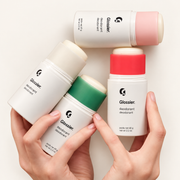 Glossier Deodorant - cztery białe sztyfty dezodorantu z wkładami w kolorze kremowym, różowym, zielonym i czerwonym trzymane w dłoniach | Ellemania