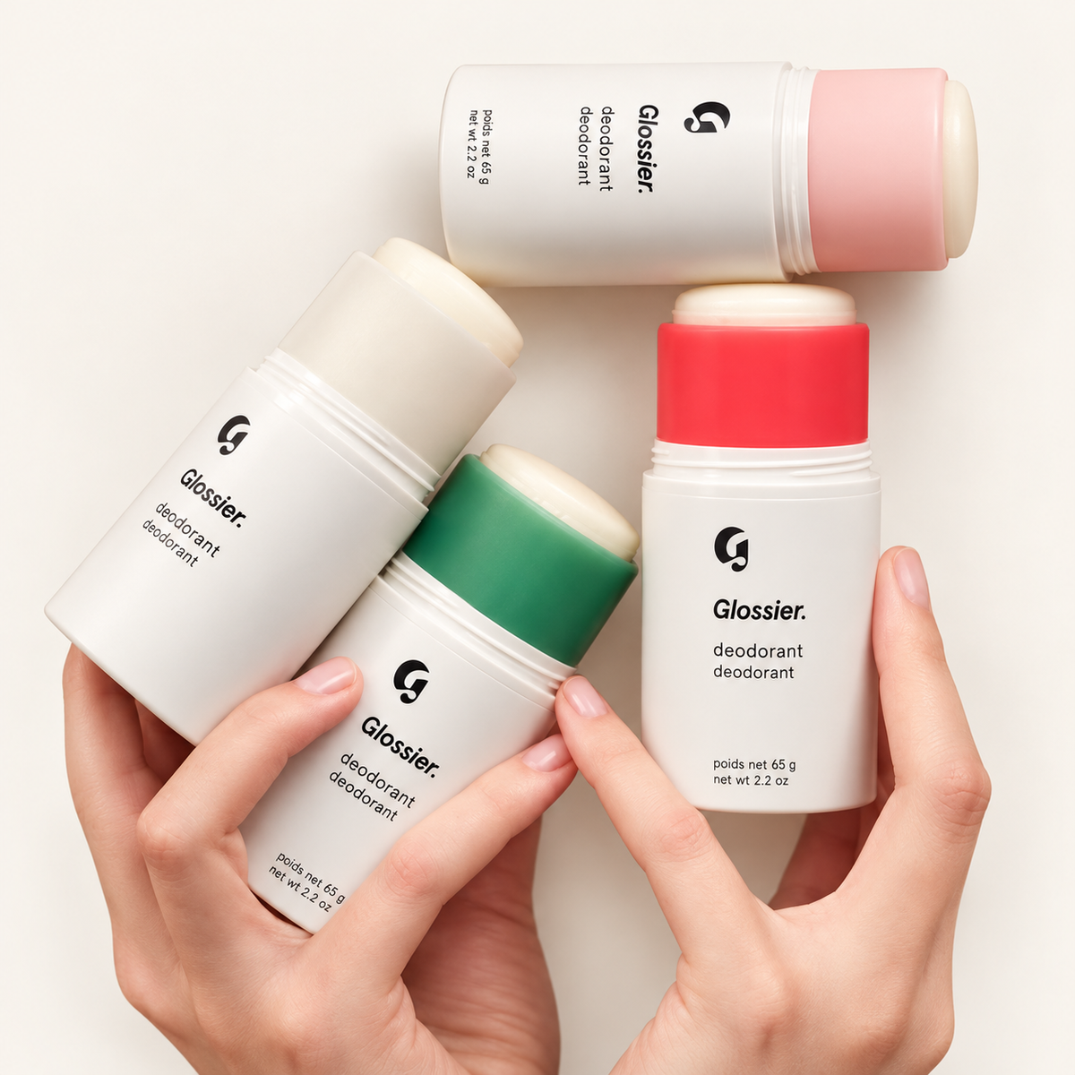 Glossier Deodorant - cztery białe sztyfty dezodorantu z wkładami w kolorze kremowym, różowym, zielonym i czerwonym trzymane w dłoniach | Ellemania