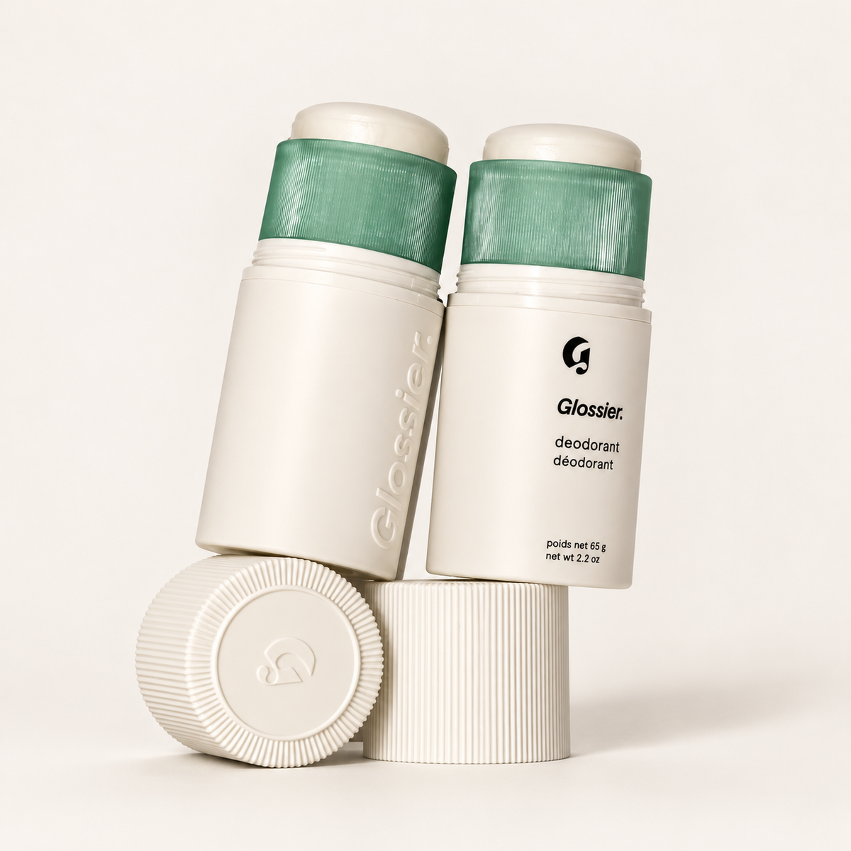 Glossier Deodorant - dwa kremowe sztyfty z zielonymi wkładami oparte o ułożone ryfkowane nakrętki | Ellemania