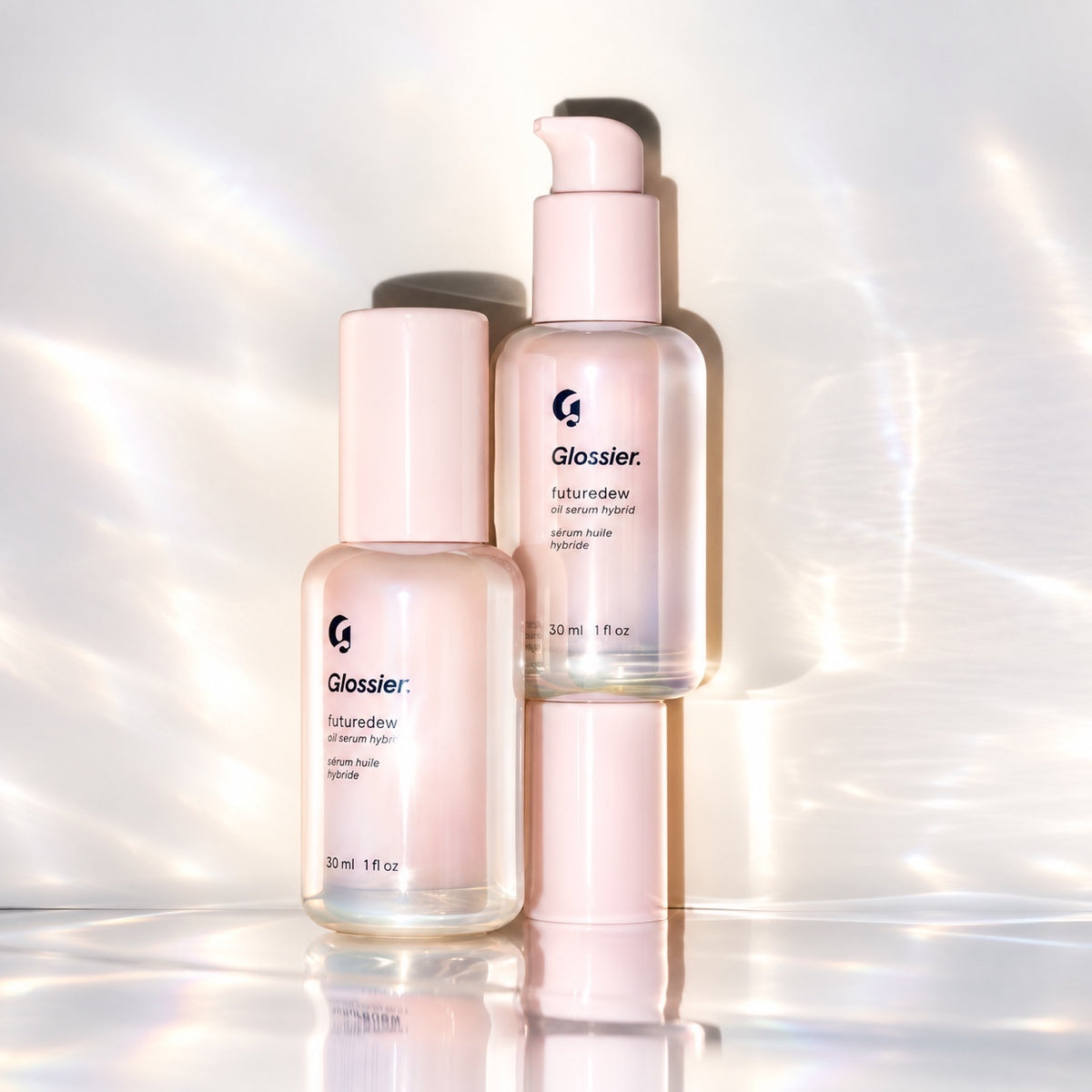 Glossier Futuredew Oil Serum Hybrid 30 ml - dwie butelki, jedna z pompką, w jasnym świetlistym kadrze z refleksami, kompozycja zdjęciowa | Ellemania