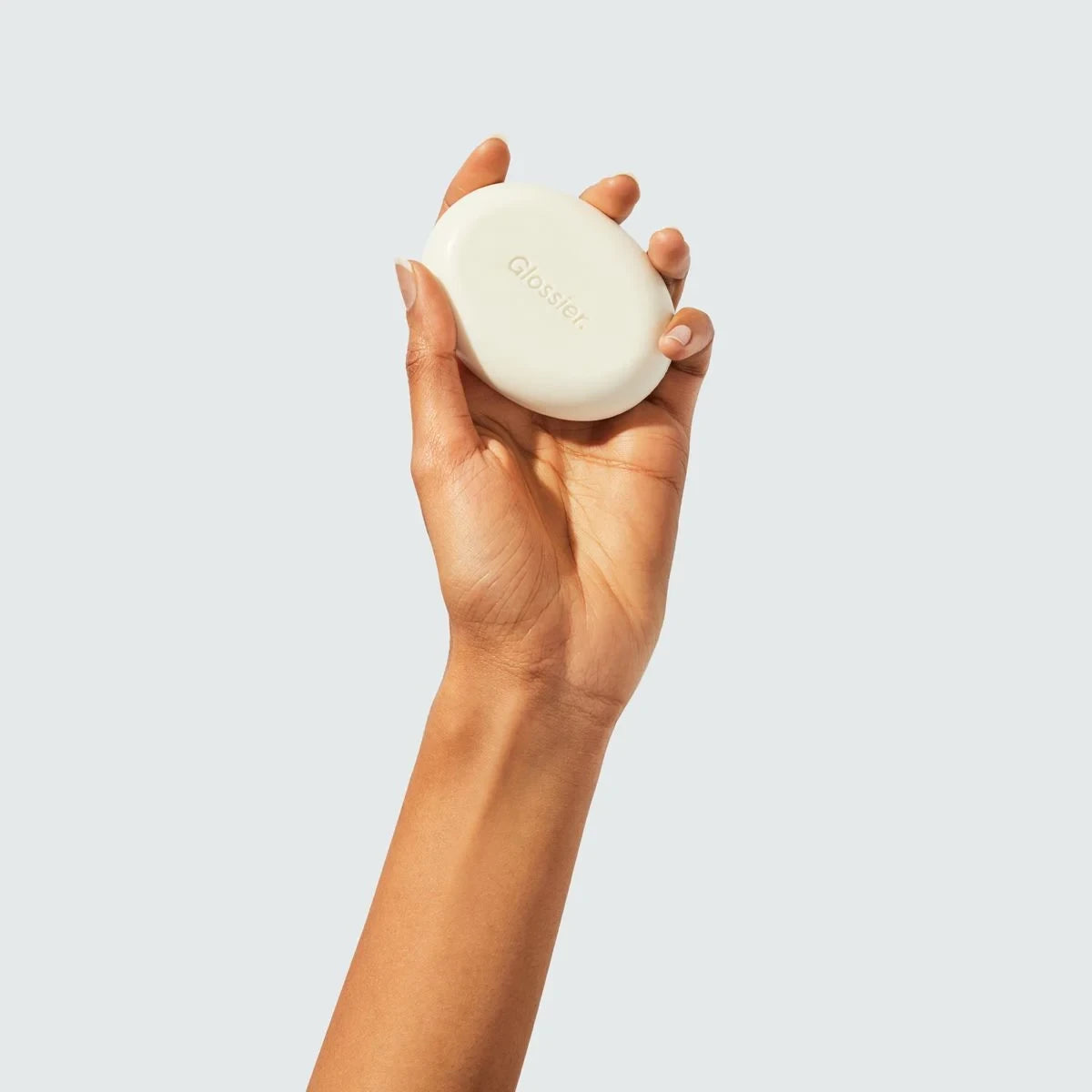 Glossier Milky Jelly Cleansing Bar - dłoń trzymająca kremową kostkę myjącą na jasnoszarym tle | Ellemania