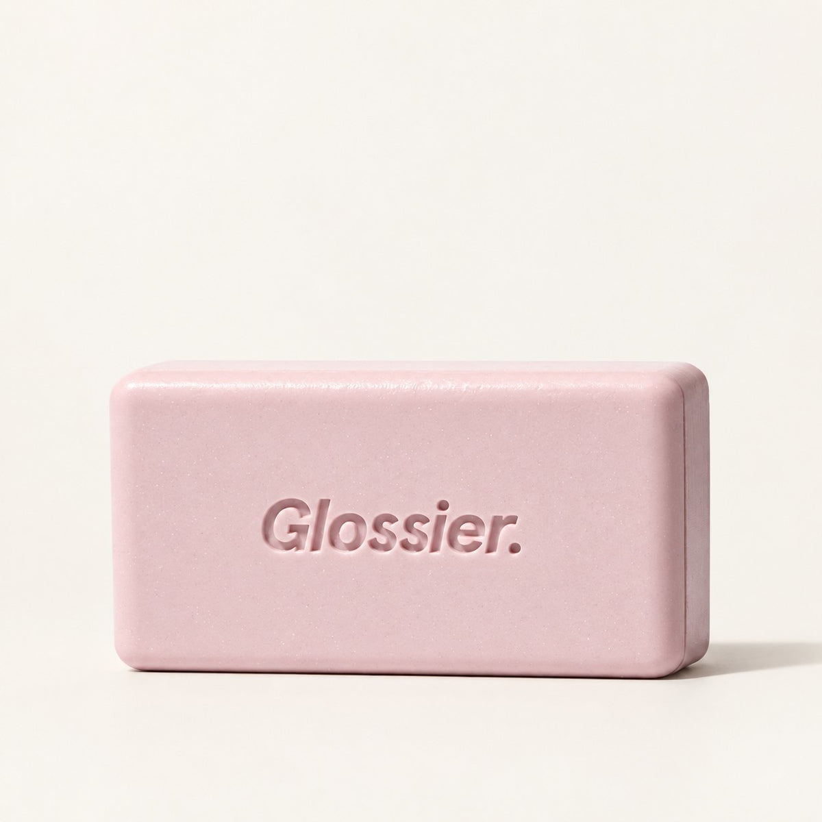 Glossier Body Hero Exfoliating Bar 141 g - kostka w kolorze różowo-fioletowym z wytłoczonym napisem Glossier, ujęcie z boku, kremowe tło | Ellemania