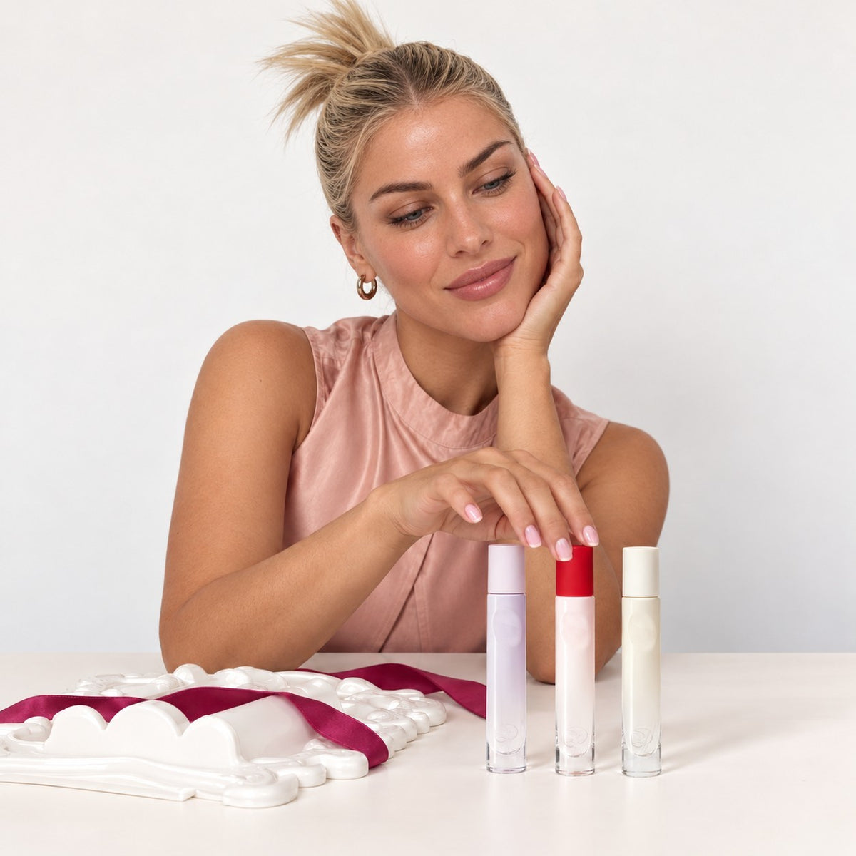 Glossier You Discovery Kit - kobieta przy stole z trzema flakonami i białym opakowaniem zestawu | Ellemania