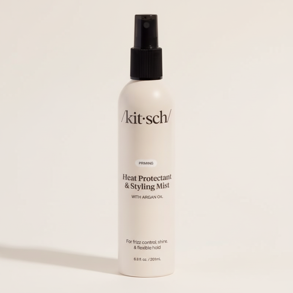 Biała butelka mgiełki termoochronnej Kitsch Heat Protectant & Styling Mist z czarnym atomizerem na jasnym tle.
