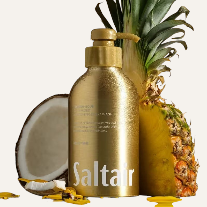 Saltair Golden Hour Oil-Infused Nourishing Body Wash 500 ml, złota butelka z pompką z przodu obok połówki kokosa i ananasa | Ellemania