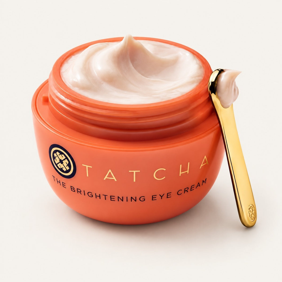 Tatcha The Brightening Eye Cream, pomarańczowy słoik z otwartym kremem i złotą łopatką z kremem | Ellemania
