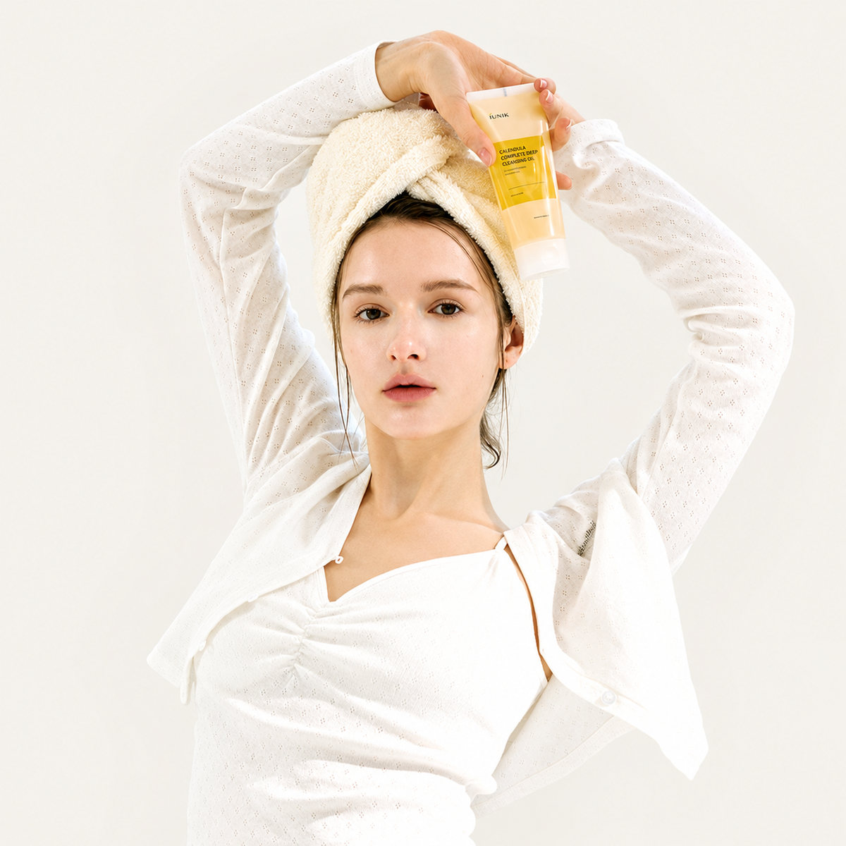 IUNIK Calendula Complete Deep Cleansing Oil - modelka z ręcznikiem na głowie trzyma żółtą tubkę nad głową | Ellemania