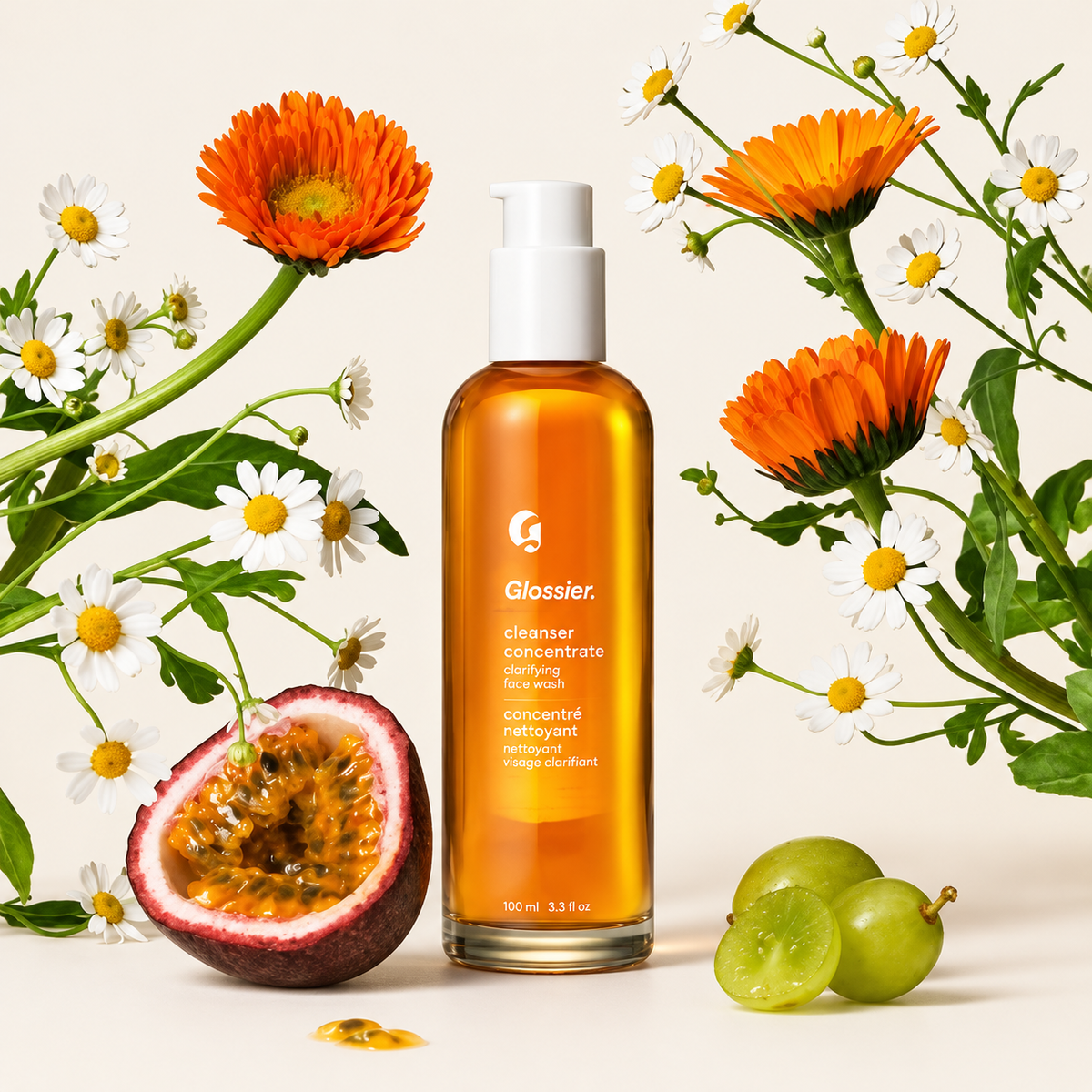 Glossier Cleanser Concentrate - butelka z pompką otoczona kwiatami i owocami na jasnym tle | Ellemania