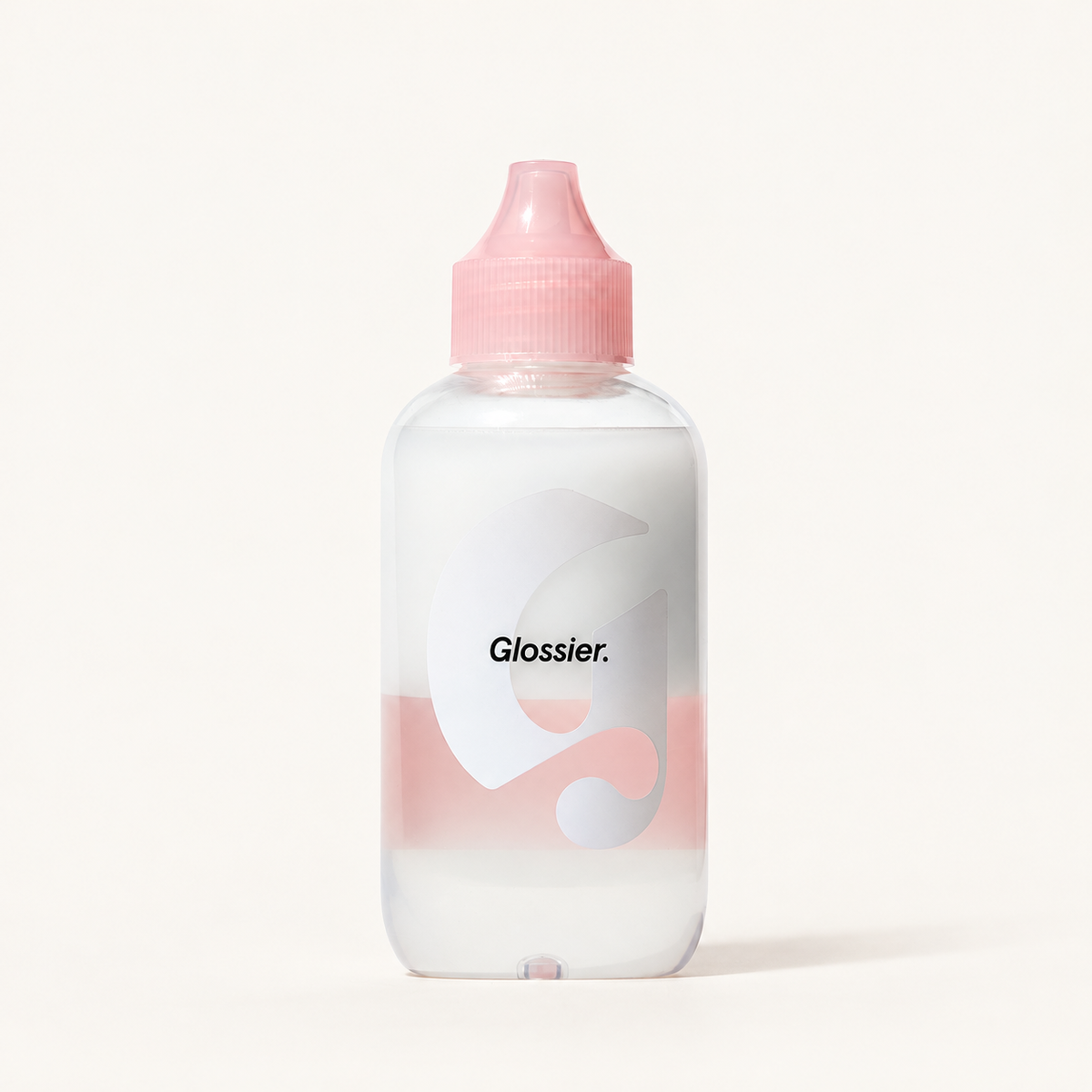 Glossier Milky Oil - przezroczysta butelka z różowym korkiem, biała warstwa u góry i różowa u dołu, logo Glossier na etykiecie, na jasnym tle | Ellemania