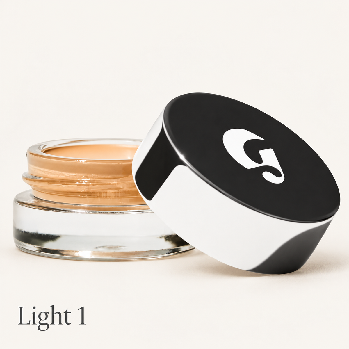 Glossier Stretch Balm Concealer - odcień Light 1, szklany słoiczek z ciepłym złocisto-beżowym korektorem i czarno-białą nakrętką z logo na jasnym tle | Ellemania