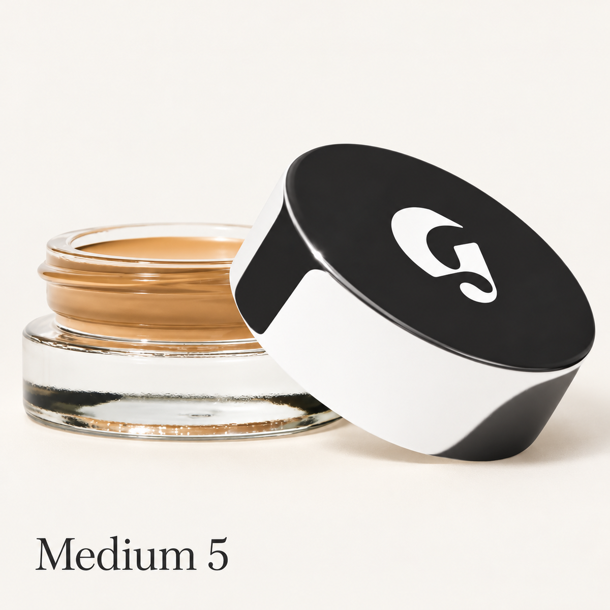 Glossier Stretch Balm Concealer - odcień Medium 5, szklany słoiczek ze złocisto-brązowym korektorem i czarno-białą nakrętką z logo na jasnym tle | Ellemania