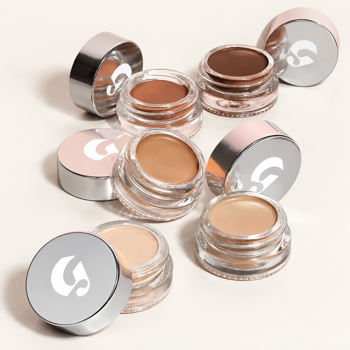 Glossier Stretch Balm Concealer - pięć słoiczków w odcieniach od jasnego beżu do ciemnego brązu, ze srebrnymi nakrętkami z logo i różowym obrzeżem, na jasnym tle | Ellemania