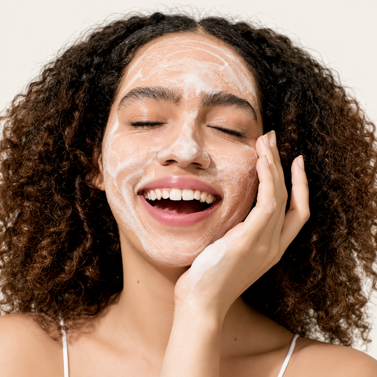 IUNIK Calendula Balancing Foam Gel Cleanser - piana na twarzy uśmiechniętej modelki, dłoń przy policzku, produkt poza kadrem | Ellemania